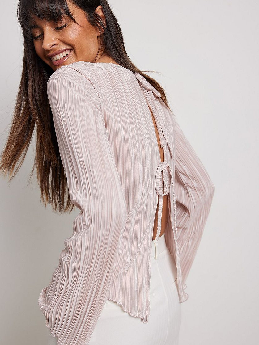Back view of model smiling, showing open-back design with tie closures on pink pleated blouse