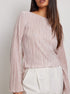 Model wearing a pale pink pleated blouse with long sleeves and boat neckline, paired with white tailored pants
