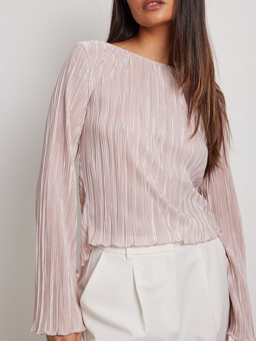 Model wearing a pale pink pleated blouse with long sleeves and boat neckline, paired with white tailored pants