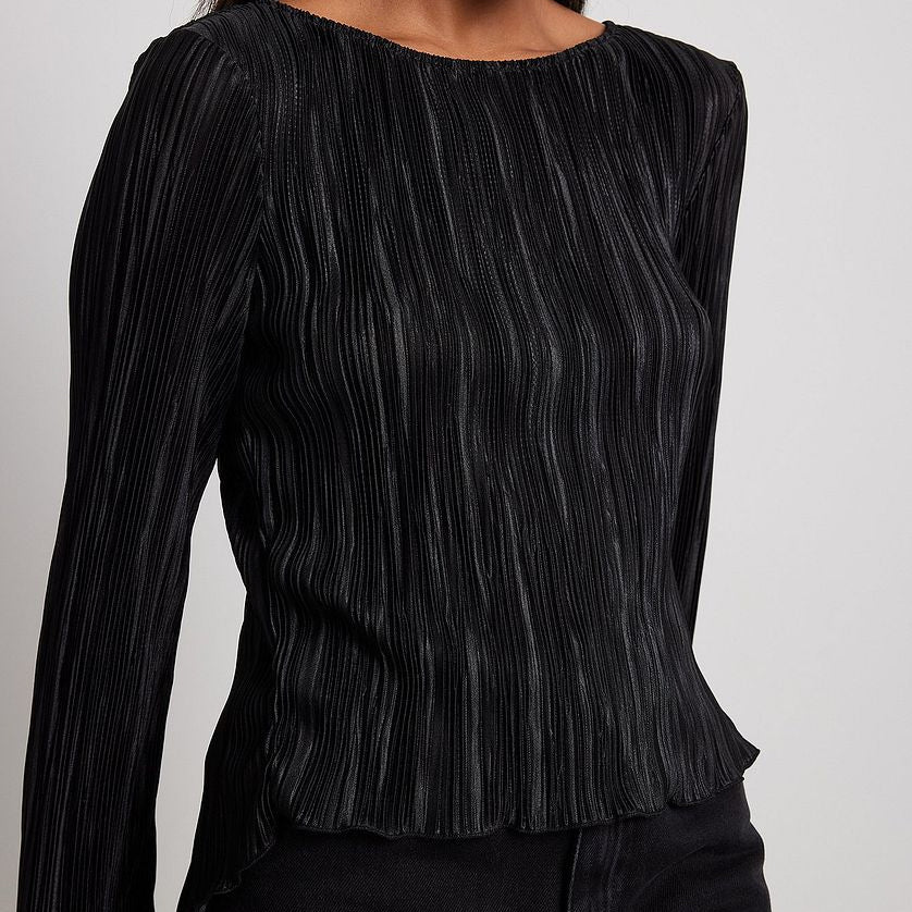 Woman wearing black pleated top with boat neckline and long sleeves, styled with black pants