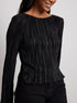 Woman wearing black pleated top with boat neckline and long sleeves, styled with black pants
