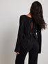 Back view of black pleated top with open-back tie details, worn with high-waisted black jeans