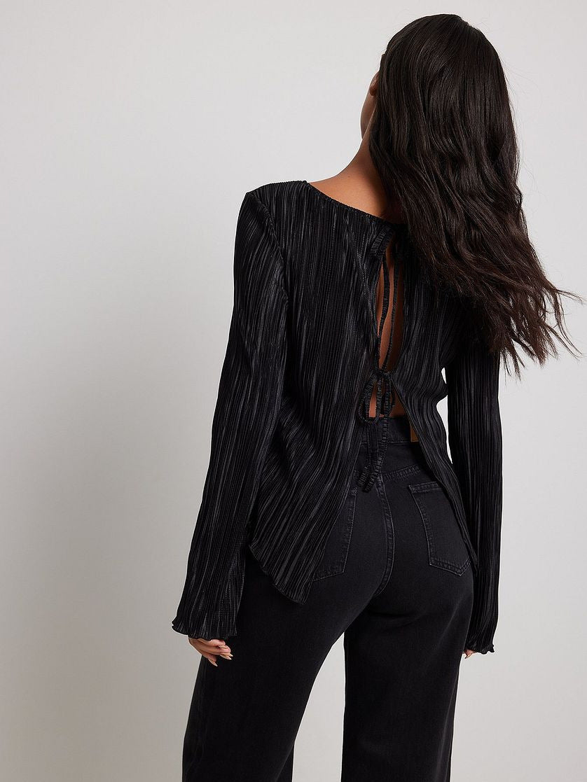 Back view of black pleated top with open-back tie details, worn with high-waisted black jeans