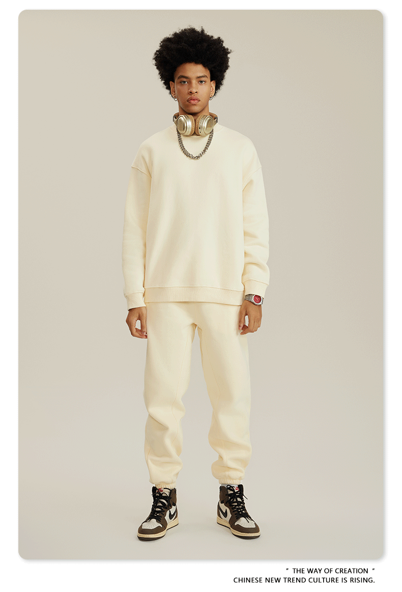 Male model in cream sweatsuit set with gold headphones draped around neck, silver chain necklace and brown/white Jordan sneakers