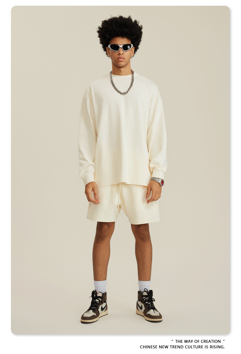 Man with afro in white sweatshirt and shorts set with sunglasses, chain necklace and sneakers