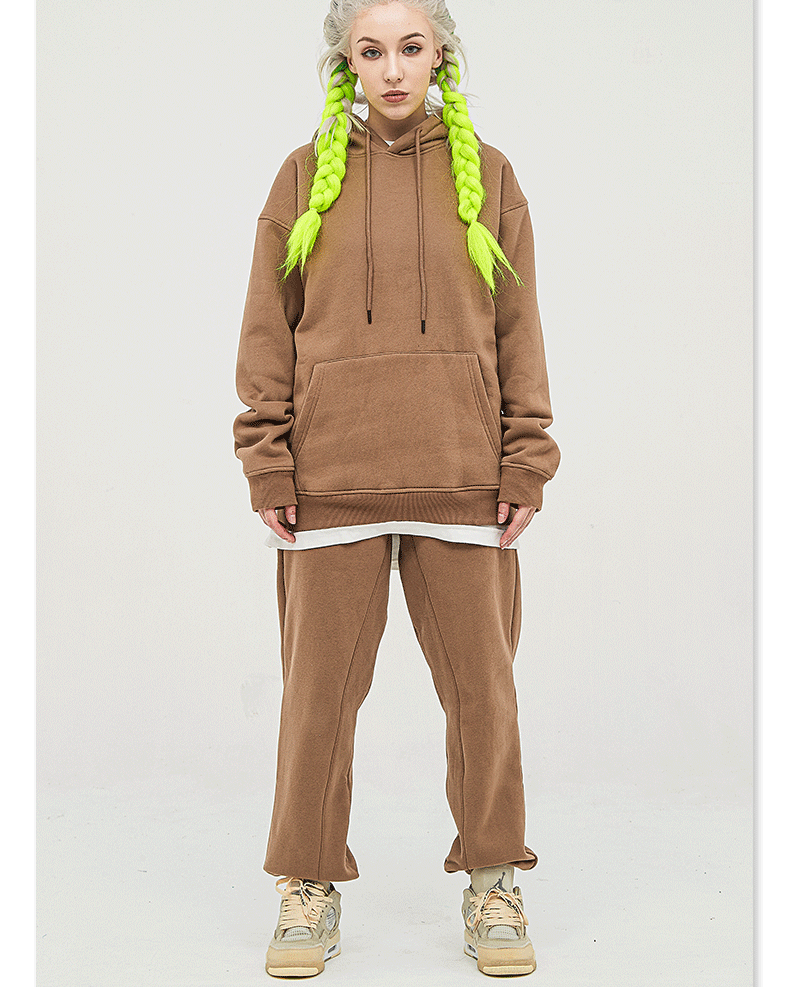 Model with platinum hair and neon green braids wearing a brown sweatsuit set with hoodie and straight-leg sweatpants, styled with beige athletic shoes