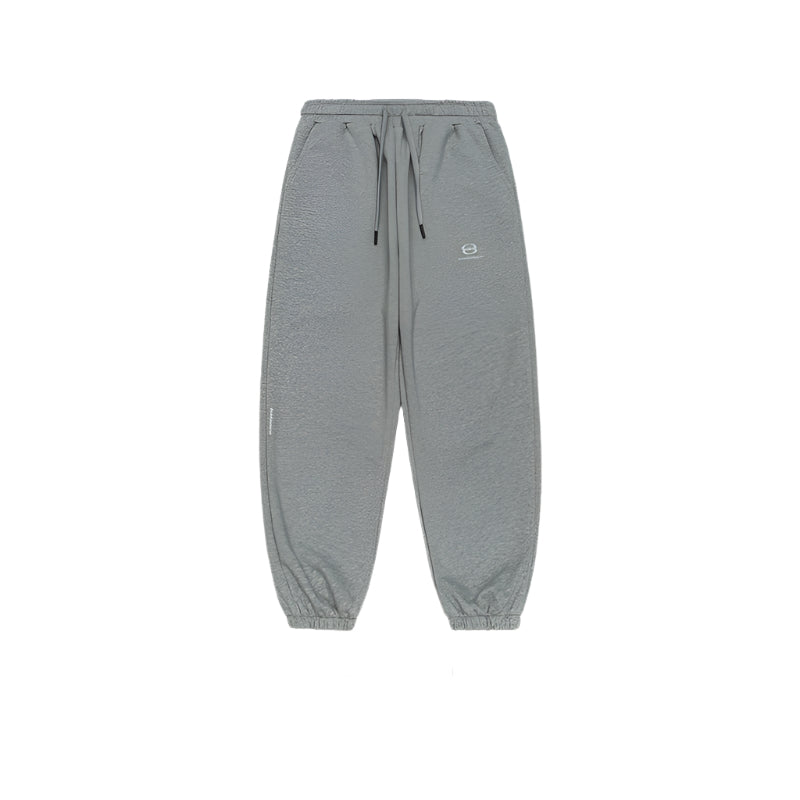 A pair of gray jogger sweatpants featuring an adjustable drawstring waist, elastic cuffs, and a small embroidered logo