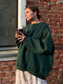 Forest green oversized sweatshirt styled with floral print skirt and holding coffee cup against brick wall