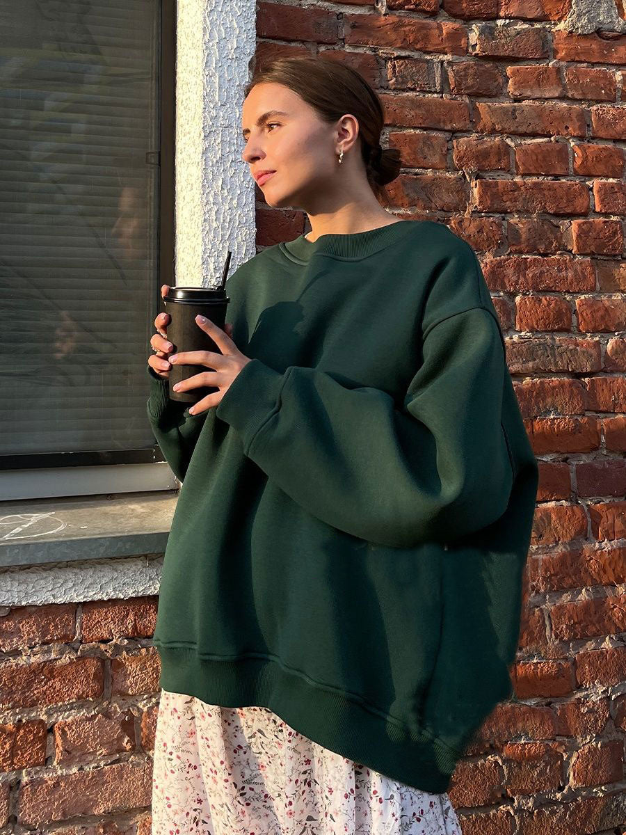 Forest green oversized sweatshirt styled with floral print skirt and holding coffee cup against brick wall