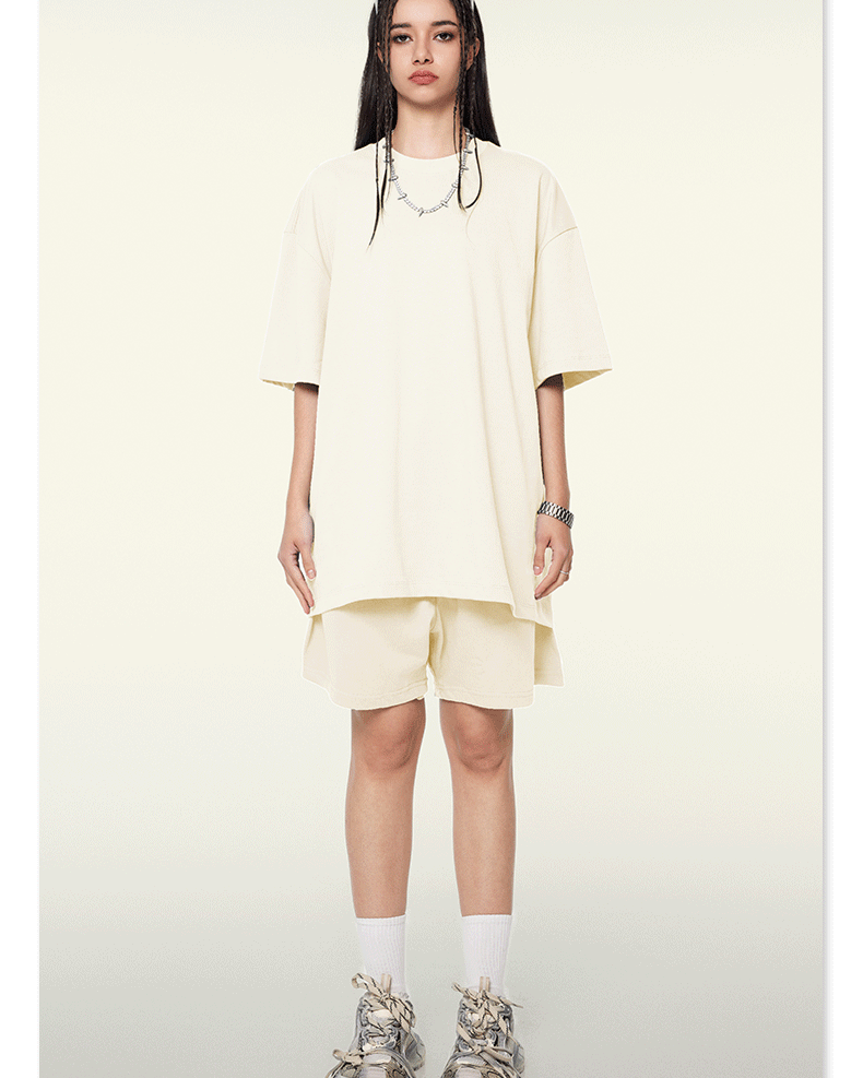 Model wearing oversized cream t-shirt and matching shorts with white socks and chunky sneakers against cream background