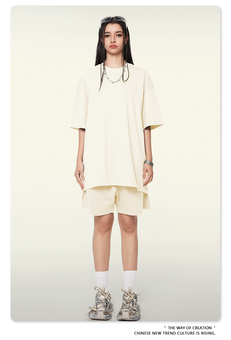 Model wearing oversized cream t-shirt and matching shorts with white socks and chunky sneakers against cream background