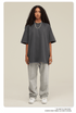 Woman wearing charcoal gray oversized t-shirt with light gray sweatpants, white sneakers and beaded necklace against neutral background