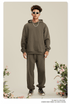Man in olive green hoodie and matching pants with afro hair standing amid floral arrangements