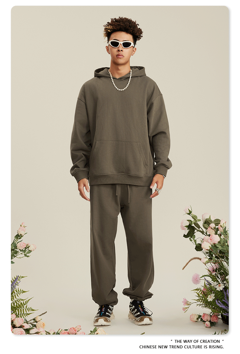 Man in olive green hoodie and matching pants with afro hair standing amid floral arrangements