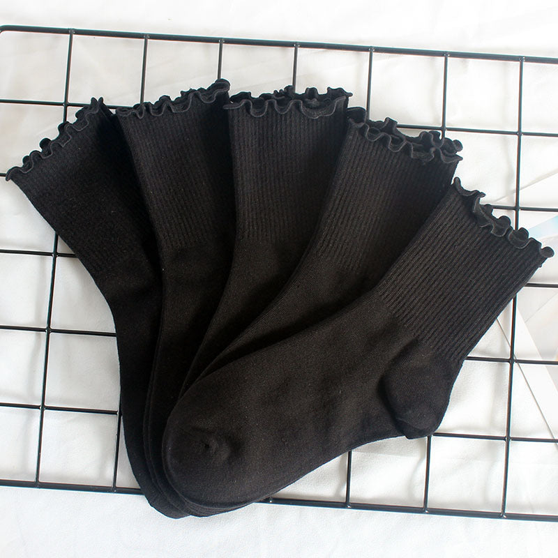 Fan display of black cotton ankle socks with ruffle edge trim arranged on metal grid, showcasing ribbed texture and decorative cuffs