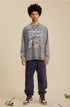 A male model wears a gray "RECOLLECT" sweatshirt with a colorful collage print, navy sweatpants, and sneakers, standing relaxed