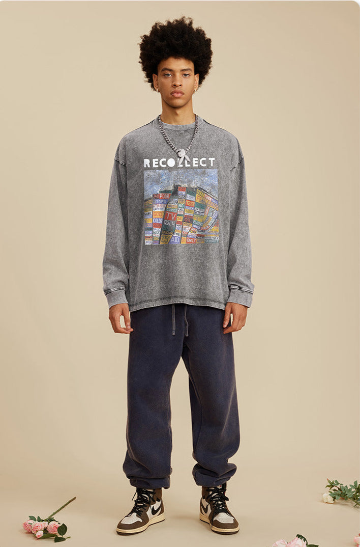 A male model wears a gray "RECOLLECT" sweatshirt with a colorful collage print, navy sweatpants, and sneakers, standing relaxed