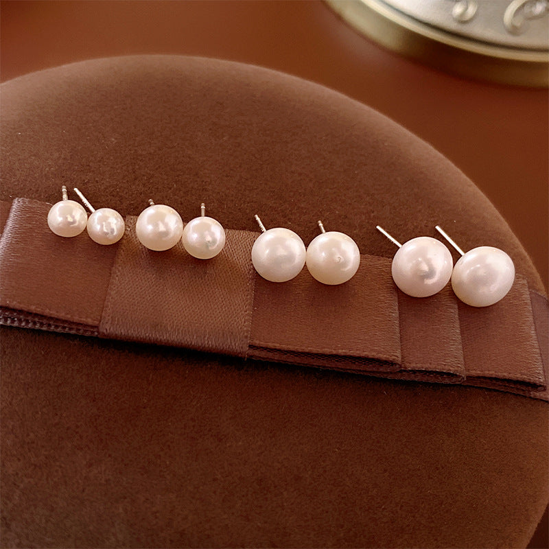 Set of four pairs of white pearl stud earrings in graduating sizes displayed on brown velvet fabric