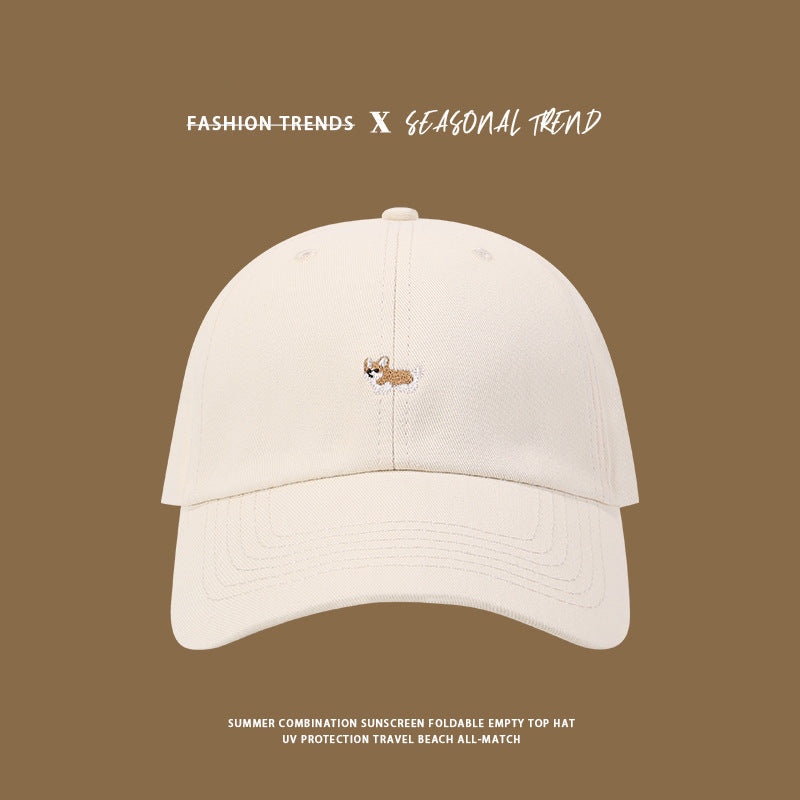 White baseball cap featuring tiny embroidered corgi dog logo against brown background