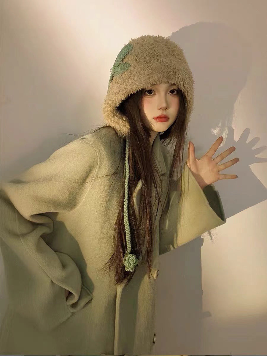 Beige plush winter hat with mint green accent and braided cord, styled with sage green sweater