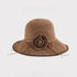 A khaki woven sun hat with a matching crochet flower and decorative ties, featuring a structured yet foldable design.