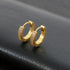 Pair of gold tone pave crystal huggie hoop earrings displayed on black leather surface, showing detailed small stone setting