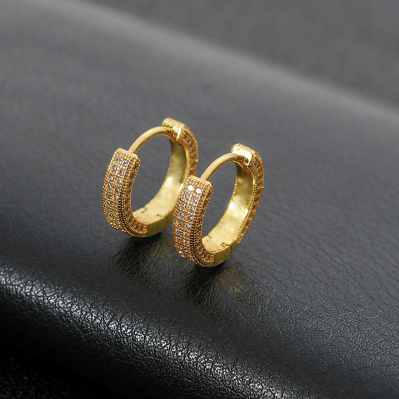 Pair of gold tone pave crystal huggie hoop earrings displayed on black leather surface, showing detailed small stone setting