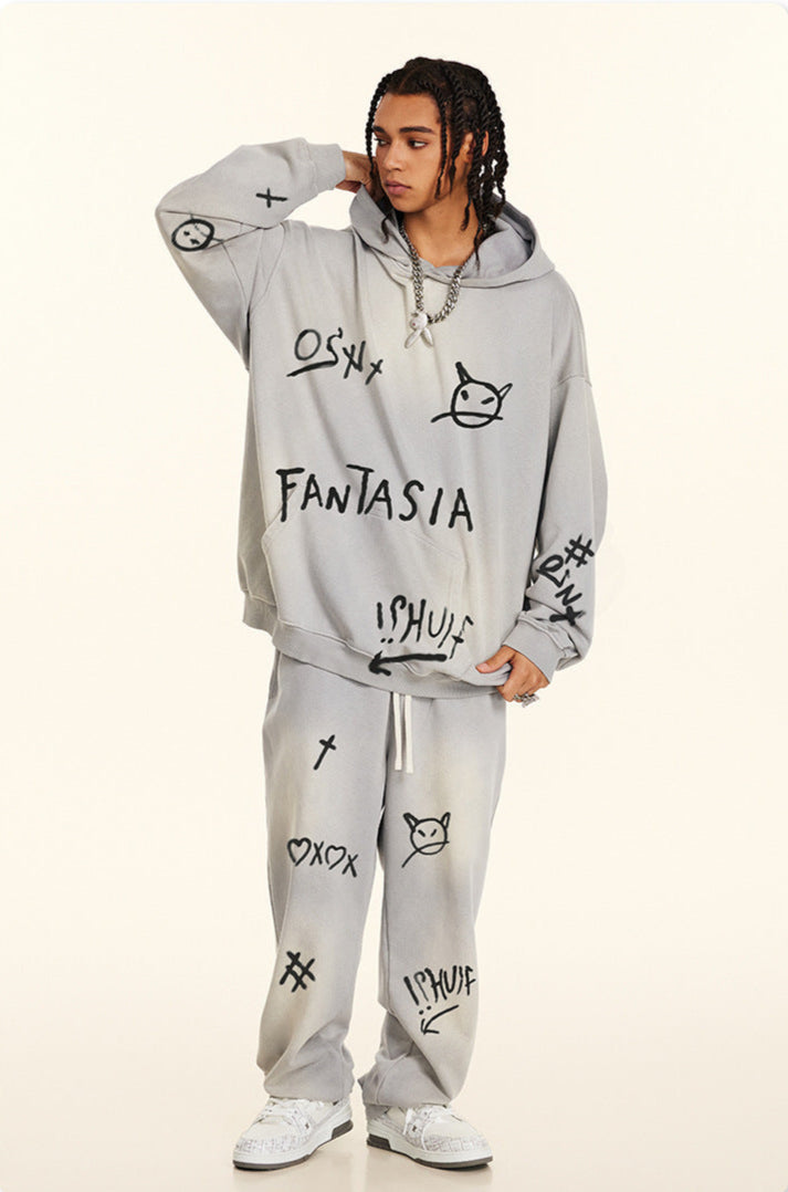 Model posing in light gray graffiti hoodie and matching sweatpants featuring hand-drawn symbols and text, wearing silver chain necklace