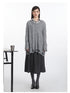 Grey cable-knit V-neck sweater with distressed hem details, layered over black and white striped collared shirt and charcoal wool midi skirt. Styled with grey ribbed tights and black leather pumps