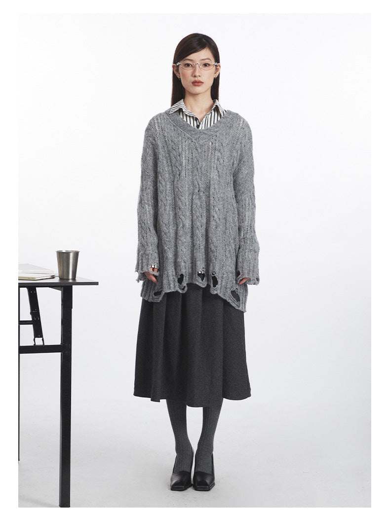 Grey cable-knit V-neck sweater with distressed hem details, layered over black and white striped collared shirt and charcoal wool midi skirt. Styled with grey ribbed tights and black leather pumps