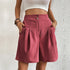 Model wearing magohany pleated shorts with dual button closure and side pockets, paired with white crop top