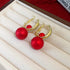 A pair of gold hoop earrings with dangling red matte pearls is displayed on a jewelry case