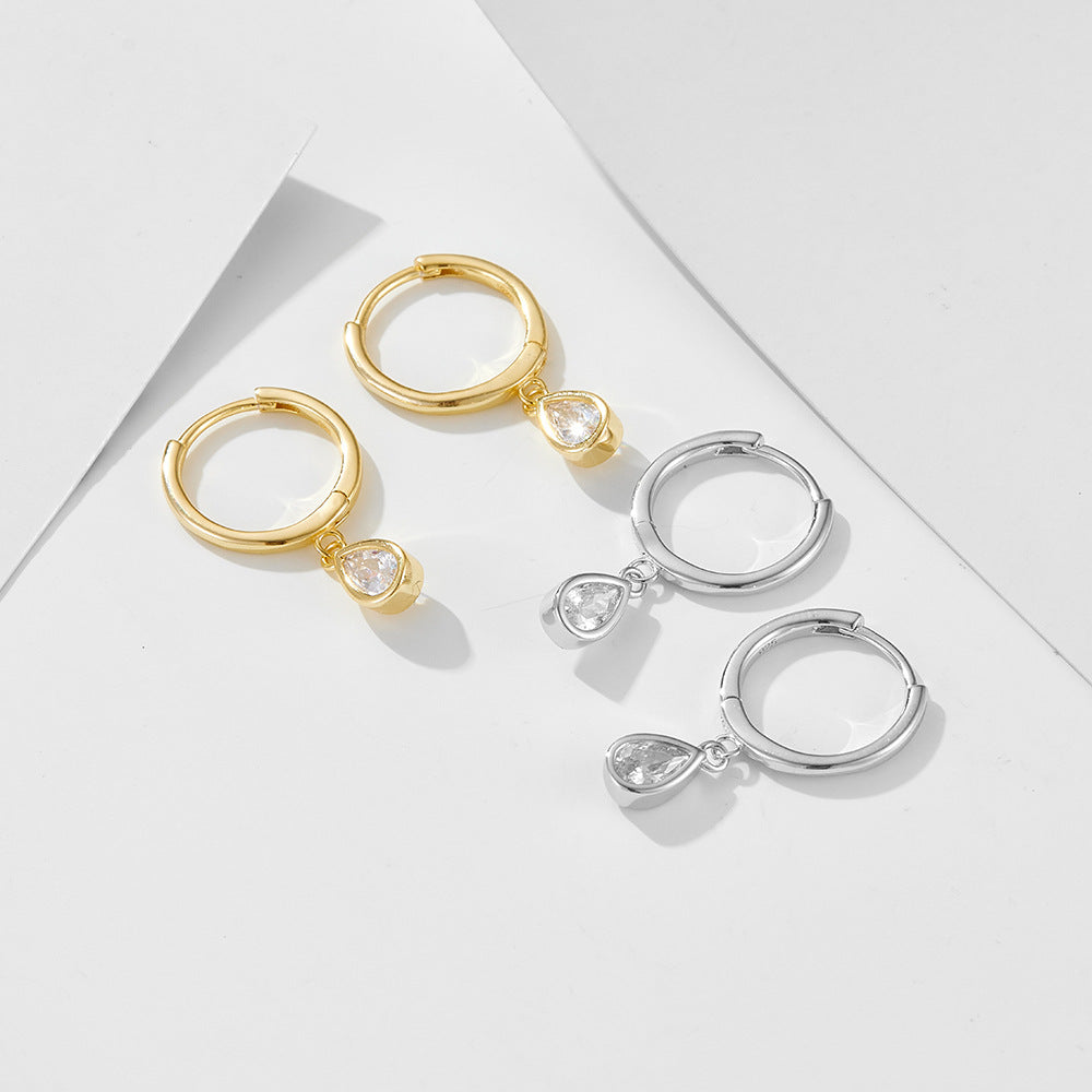 Gold and silver huggie hoops with teardrop crystal pendants arranged on geometric white background