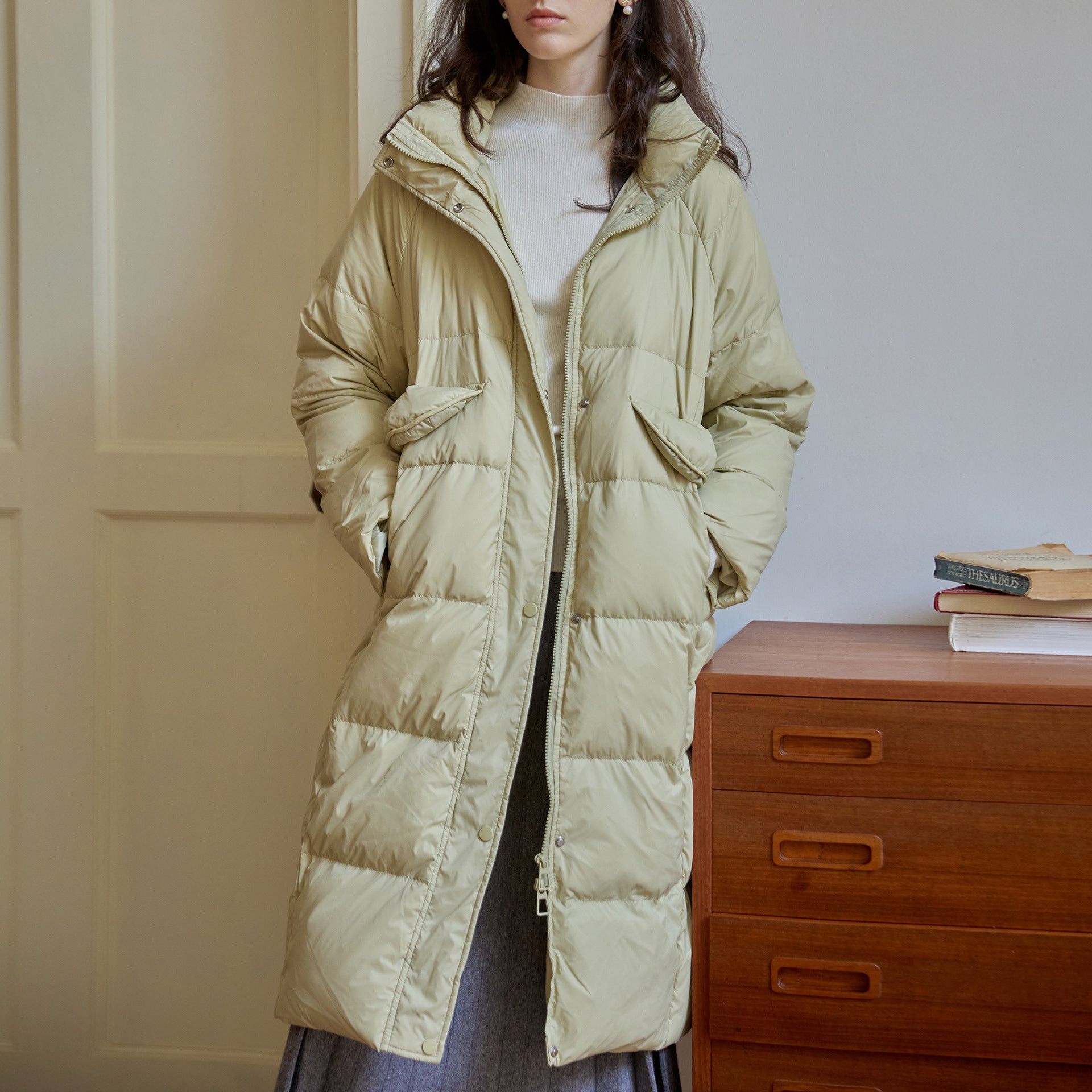 Pale yellow long puffer coat with oversized fit and utility pockets, styled with cream sweater and grey skirt