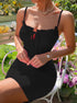 A woman in black ribbed mini dress with ruched tie front sits in garden chair surrounded by flowering plants