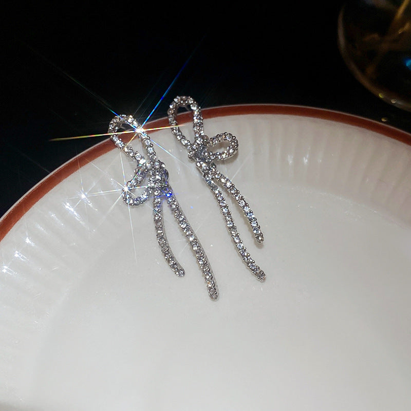 Crystal-encrusted silver bow drop earrings displayed on white plate, capturing dramatic sparkle and movement