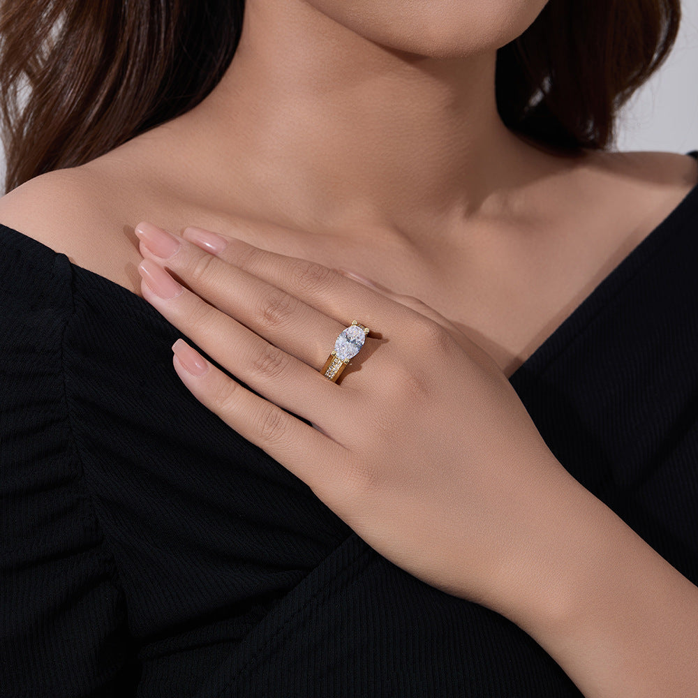 A woman wearing gold oval diamond engagement ring on her finger against black top background