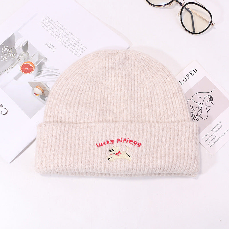 Cream ribbed knit beanie with Lucky Pipiegg puppy embroidery on white product display with glasses