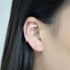 A woman wearing two gold rainbow huggie hoop earrings in her ear, close-up against black hair