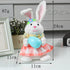 White plush bunny wearing a pink checkered dress and flower headband, holding a blue Easter egg, with labeled size dimensions of 24cm height and 11cm width.