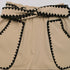 Close-up of the waistband of beige shorts featuring black lace trim and a decorative bow belt.