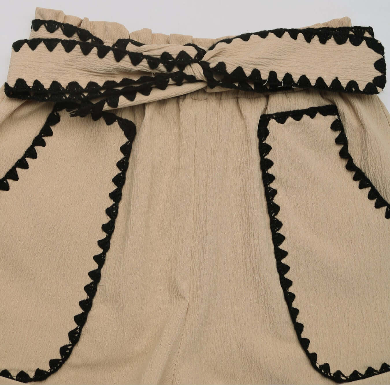 Close-up of the waistband of beige shorts featuring black lace trim and a decorative bow belt.
