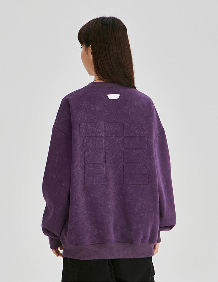 Back view of a purple oversized sweatshirt featuring a large embossed logo design, ribbed cuffs, and a casual streetwear fit