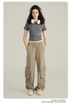 Model with curly dark hair wearing a gray crop top, beige cargo pants with zippered pockets, white headphones around neck on neutral background