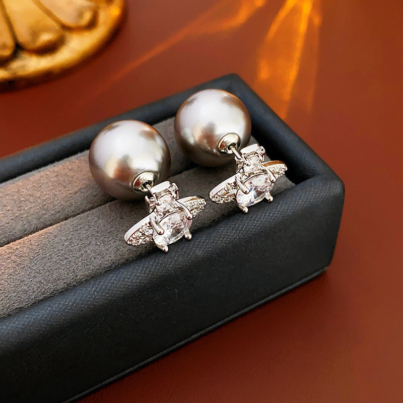 Rhodium crystal orbit earrings with pearl backing on wooden surface