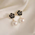 Pair of black camellia flower earrings with crystal edges and large pearl drops on white fabric background