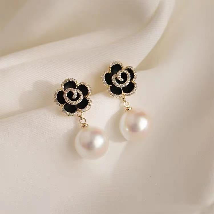 Pair of black camellia flower earrings with crystal edges and large pearl drops on white fabric background