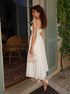 Woman in a white dress standing outside a building with green shutters.