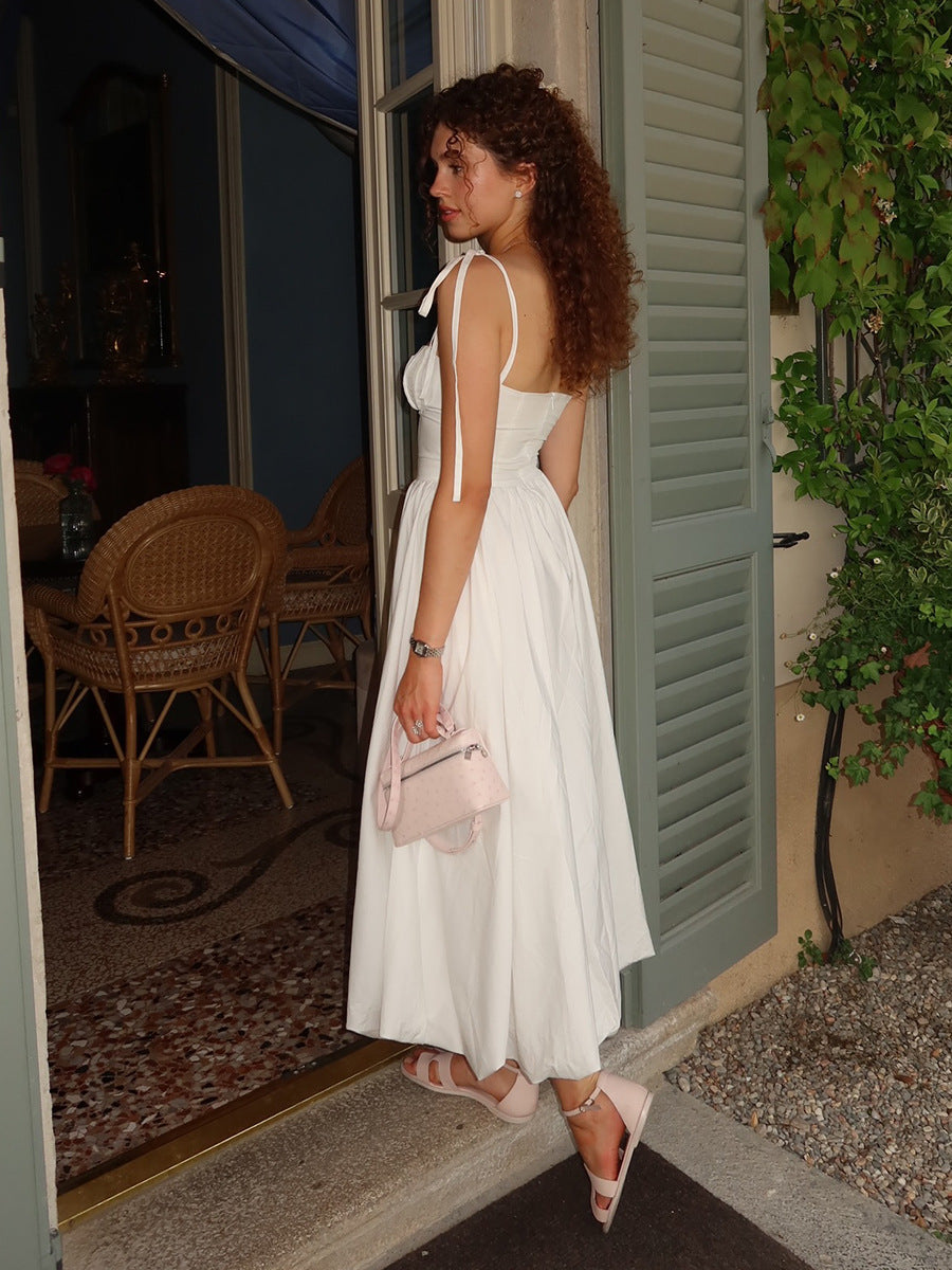 Woman in a white dress standing outside a building with green shutters.