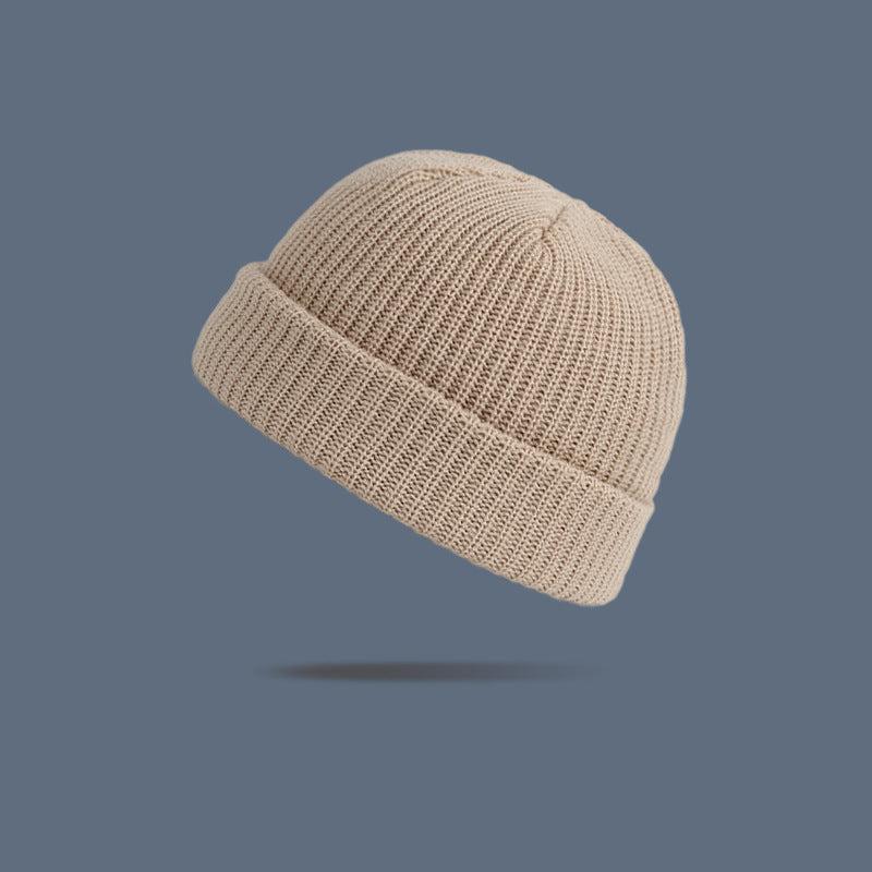 A cream ribbed knit beanie with folded cuff floating against slate gray background, displaying classic winter hat silhouette